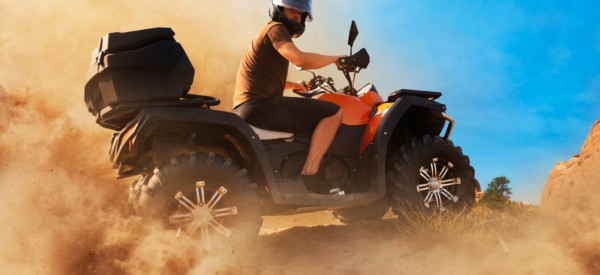 Atv in dust clouds, sand quarry on background. Male driver in helmet on quad bike in sandpit