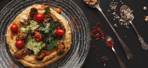 Chickpea hummus with mussels and vegetables in stylish bowl. Healthy traditional vegetarian beans pasta with olive oil and fresh pita bread served on black table background